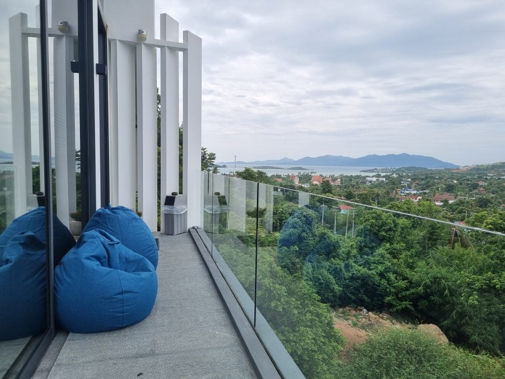 Panoramic view from the Sunrise Suite balcony featuring blue bean bags, overlooking lush greenery and distant mountains.