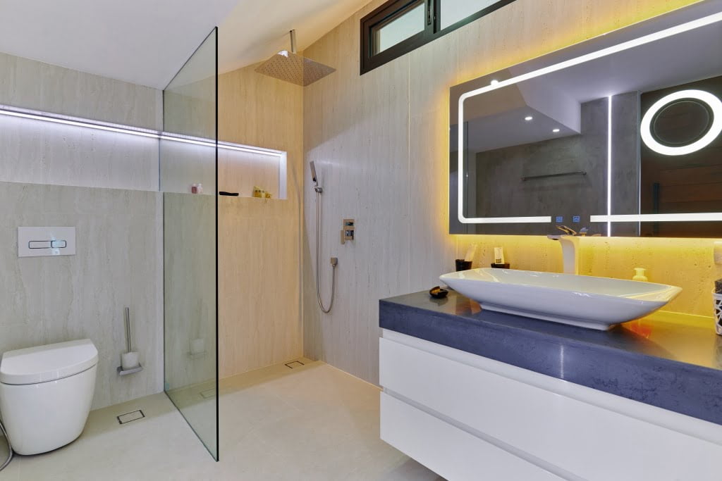 Modern bathroom with a glass shower, stylish mirror, and yellow lighting accents in Magic Suites.