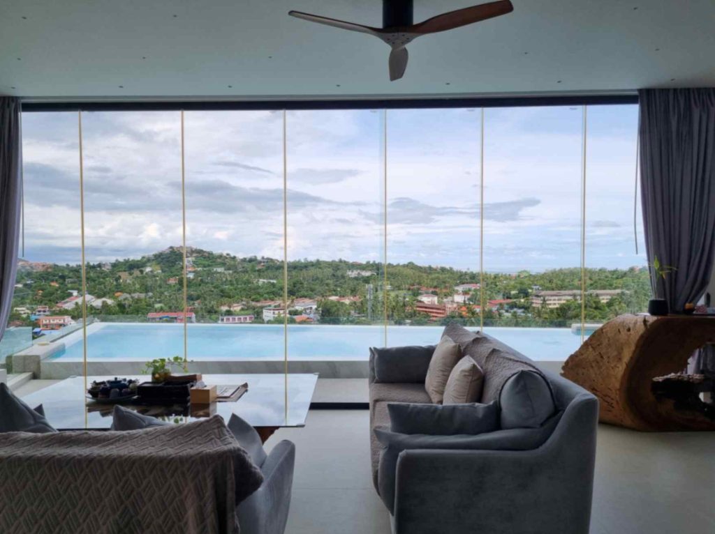Luxurious suite with floor-to-ceiling windows overlooking a pool and panoramic views of Koh Samui.