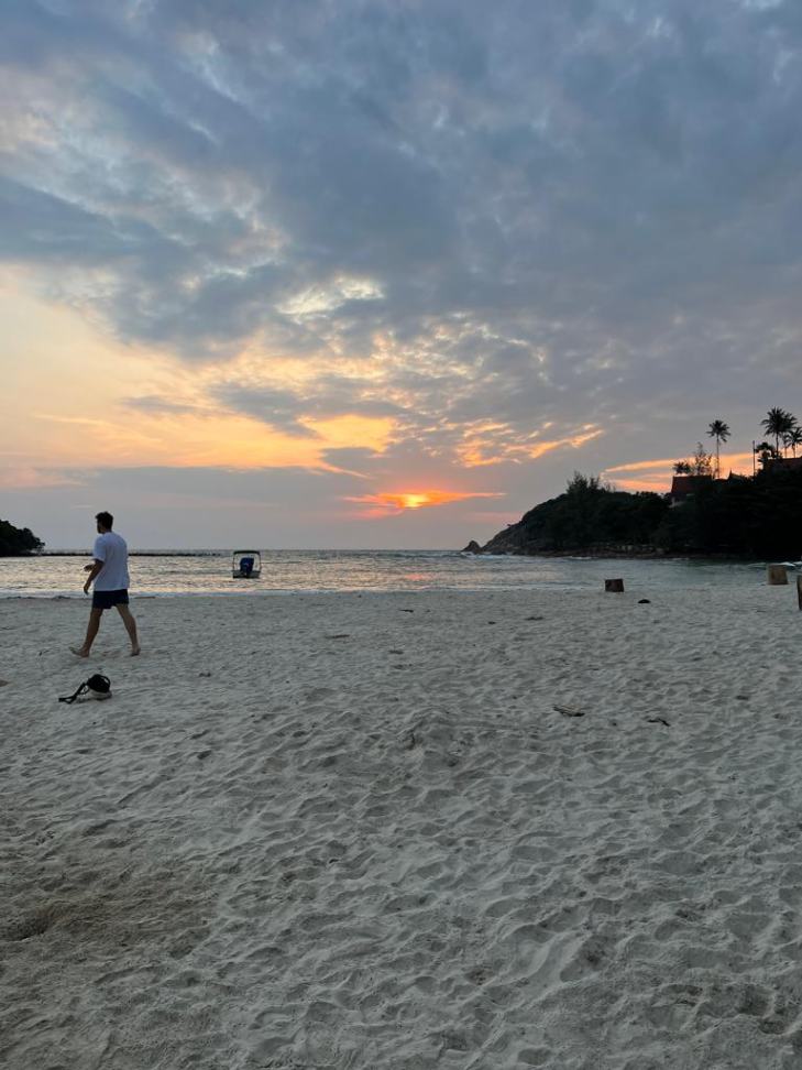 Man walking on sandy beach at sunset with dramatic clouds in Koh Samui.