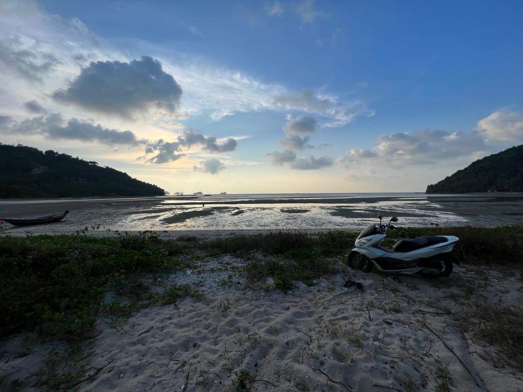 Serene Koh Samui beach at dusk with a motorbike on the sand and dramatic sky over tranquil waters.