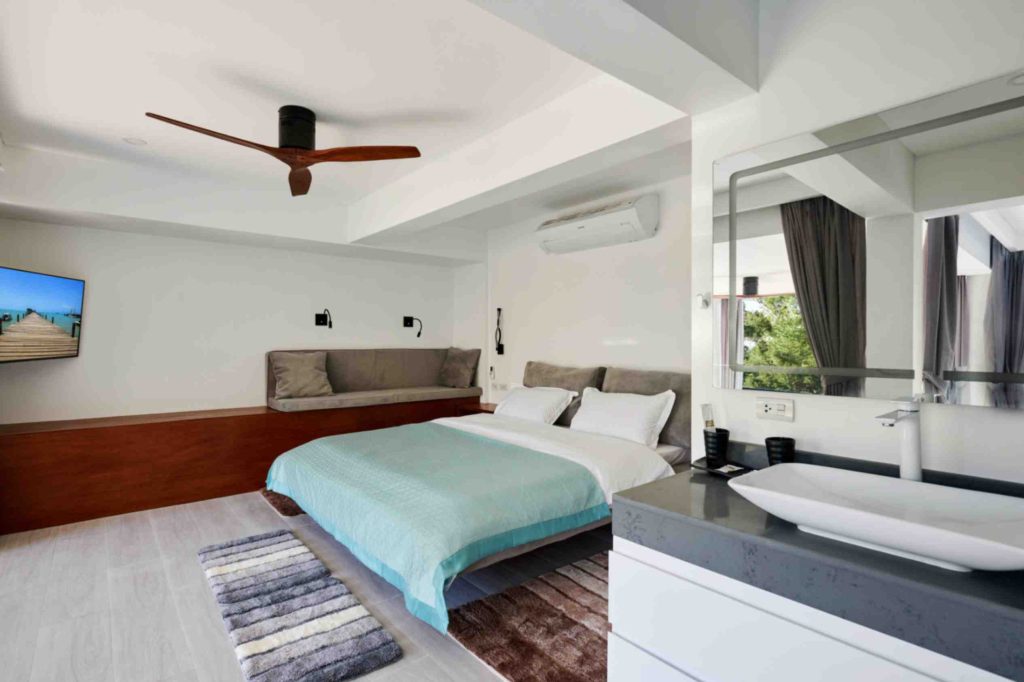 Elegantly designed bedroom, featuring an air conditioner, TV, and bathroom sink, in Magic Suites.
