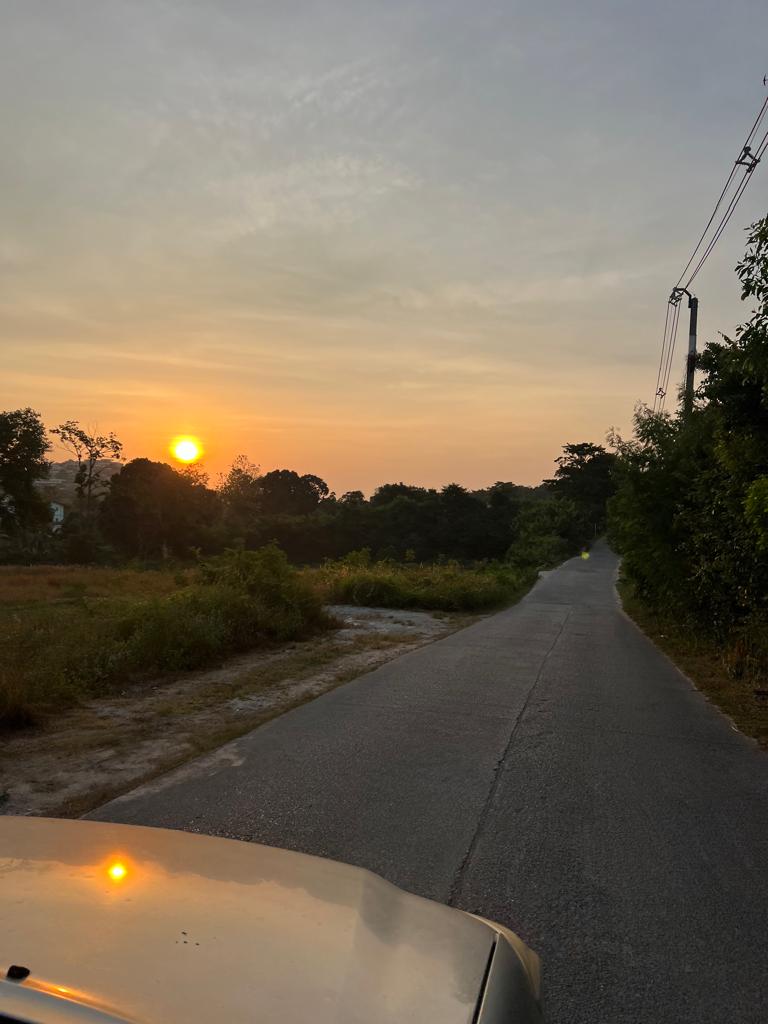 Golden sunset along a quiet road in Koh Samui, reflecting off a car hood.