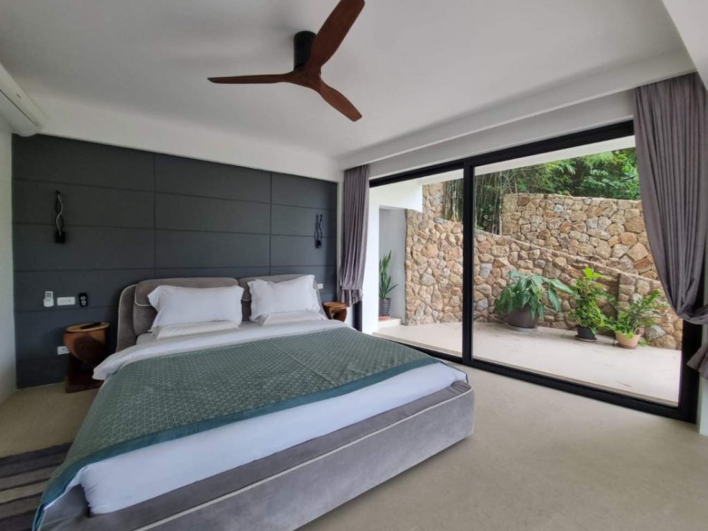 Modern Garden Suite bedroom with a large bed, ceiling fan, and sliding doors opening to a garden.