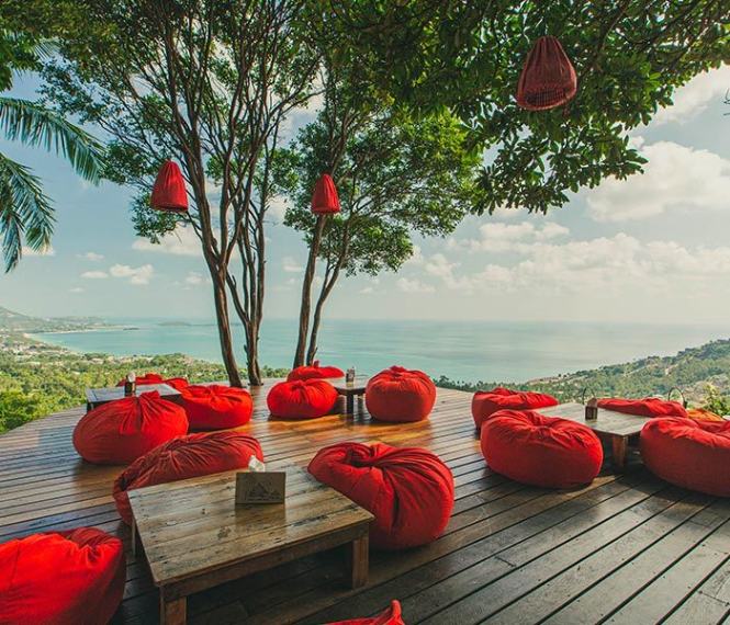Relaxing outdoor lounge at Jungle Club with red bean bags and a panoramic sunrise view amidst lush greenery.