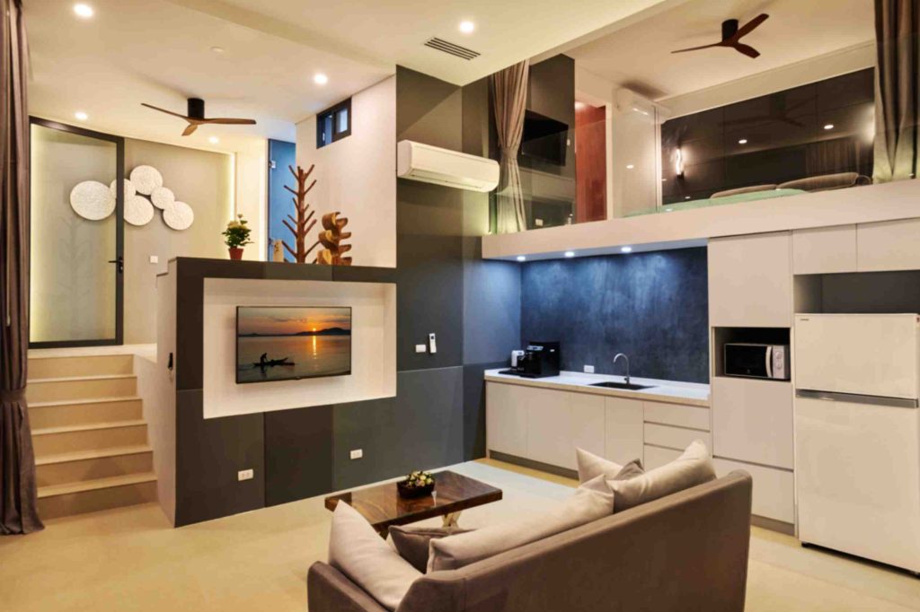 Modern garden suite living room with a gray sectional sofa, a central wooden coffee table, and an integrated kitchen.